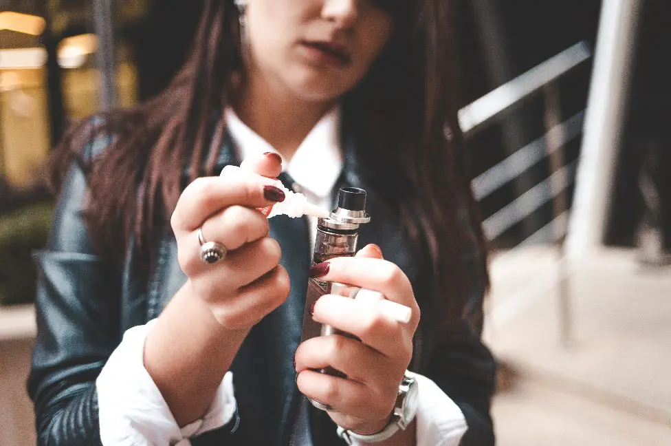 Une femme recharge du liquide dans une cigarette électronique en gros plan